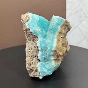 May include: A rough-hewn rock formation featuring a vibrant turquoise mineral vein running through its center. The stone has a textured, porous surface with shades of tan and gray, creating a striking contrast with the bright blue.