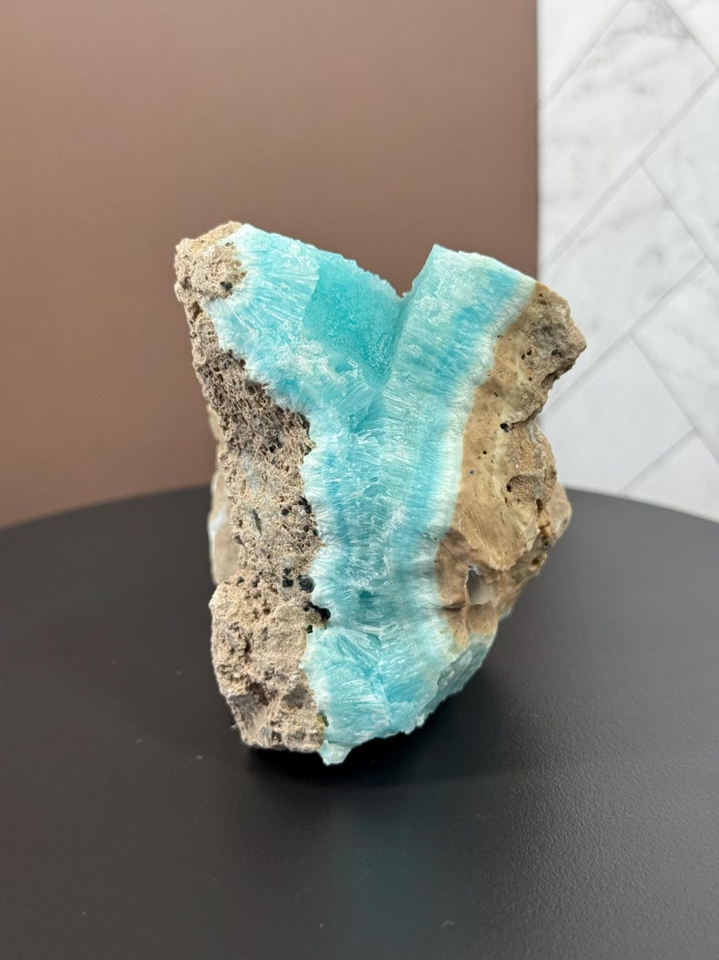 May include: A rough-hewn rock formation featuring a vibrant turquoise mineral vein running through its center. The stone has a textured, porous surface with shades of tan and gray, creating a striking contrast with the bright blue.