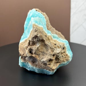 May include: A rough, natural stone with layers of light blue and tan colors. The stone has a textured surface with visible holes and imperfections. The blue layers appear to be crystalline, contrasting with the rougher, earthy tones of the rest of the stone.