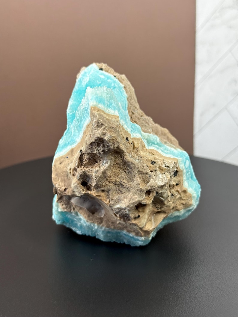 May include: A rough, natural stone with layers of light blue and tan colors. The stone has a textured surface with visible holes and imperfections. The blue layers appear to be crystalline, contrasting with the rougher, earthy tones of the rest of the stone.