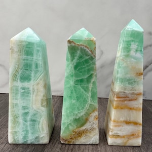 Puede incluir: Tres cristales en forma de obelisco de color verde y blanco. Los cristales son de diferentes tonos de verde y blanco, algunos con más tonos marrones. Los cristales están numerados del 1 al 3.
