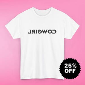 Puede incluir: Camiseta blanca con la palabra "COWGIRL" impresa en negro, al revés. Una pegatina en blanco y negro con el texto "25% OFF" está en la esquina inferior derecha. La camiseta tiene mangas cortas y cuello redondo.