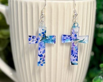 Puede incluir: Un par de pendientes de cruz plateados con un diseño floral azul y morado.