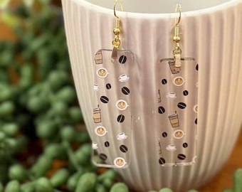 May include: A pair of gold dangle earrings with clear rectangular charms featuring a repeating pattern of coffee cups and coffee beans.