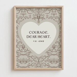 Może przedstawiać: Oprawiony wydruk z cytatem "Courage, Dear Heart" C.S. Lewisa. Tekst umieszczono w jasnoszarym kształcie serca, na tle wzorzystym w odcieniach szarości i brązu. Rama wykonana jest z jasnego drewna.