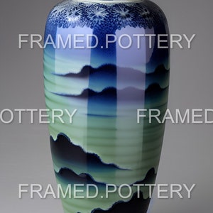 May include: A tall, glazed ceramic vase with a wide mouth and a round base. The vase features a gradient of colors, transitioning from dark blue at the top to green at the bottom, with a landscape design. The vase is on a wooden stand.