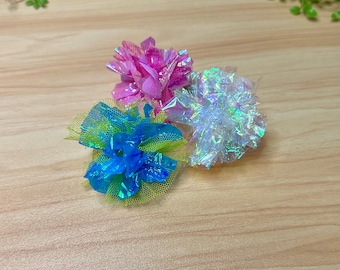 May include: Three colorful cat toys in the shape of flowers. The flowers are made of iridescent fabric and tulle. The flowers are pink, blue, and white.