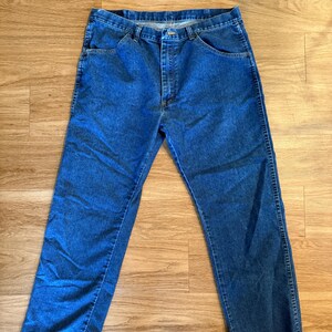 May include: Blue denim jeans with a classic five-pocket design. The jeans have a straight leg cut and a button and zipper closure. The denim has a medium wash and visible stitching.