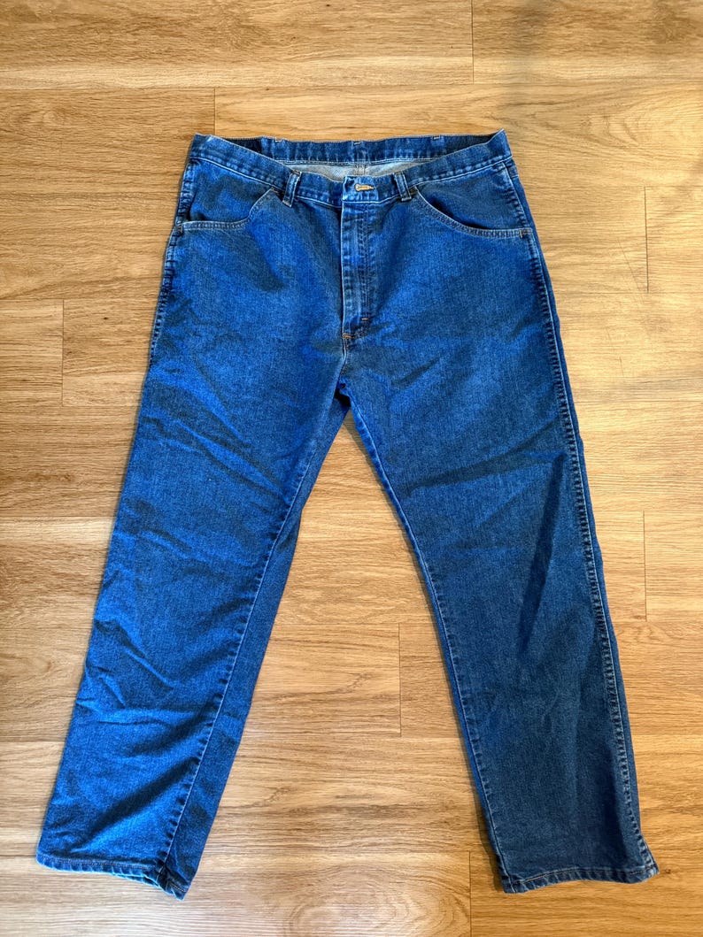 May include: Blue denim jeans with a classic five-pocket design. The jeans have a straight leg cut and a button and zipper closure. The denim has a medium wash and visible stitching.