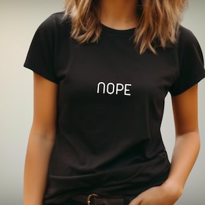 Könnte beinhalten: Ein schwarzes Kurzarm-T-Shirt mit dem Wort NOPE in weißen Großbuchstaben auf der Brustmitte. Das Kleidungsstück hat einen Rundhalsausschnitt und eine Standardpassform und besteht aus einem einfarbigen schwarzen Stoff mit glatter Textur.