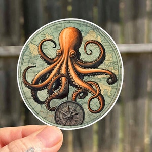 Puede incluir: Una pegatina redonda con un pulpo naranja de ocho tentáculos envueltos alrededor de un mapa del mundo vintage. Una brújula con una esfera negra y agujas plateadas se encuentra en el centro del mapa.