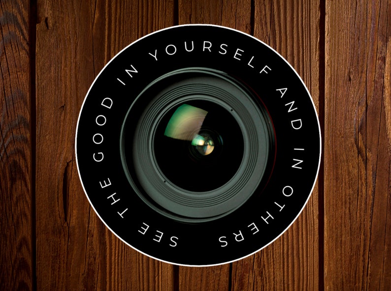 Puede incluir: Un objetivo de c&aacute;mara en blanco y negro con el texto "See the good in yourself and in others" alrededor del borde.