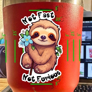 May include: A red stainless steel tumbler with a sloth graphic and the text "Not Fast Not Furious".