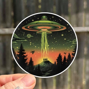 May include: A sticker featuring a green UFO with yellow lightning bolts descending from it. The UFO is flying over a dark forest with a mountain in the background. The sky is a gradient of orange, yellow, and green.