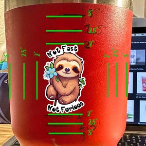 May include: Red stainless steel tumbler with a sloth graphic and the text "Not Fast Not Furious". The tumbler has measurements marked in inches.