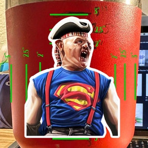 K&ouml;nnte beinhalten: Ein bunter Aufkleber mit einer Comicfigur, die ein rot-wei&szlig;-blaues Superman-Kost&uuml;m mit einem rot-wei&szlig; gestreiften Hut tr&auml;gt. Die Figur tr&auml;gt rote Hosentr&auml;ger und hat einen &uuml;berraschten Gesichtsausdruck.