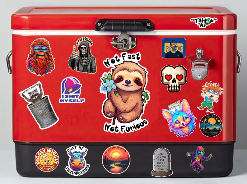 May include: A red metal cooler with various stickers, including a sloth holding a flower, a skull with hearts, a raccoon in a trash can, a Taco Bell logo, a skeleton with the text "Stay Positive", and a sunset landscape. The cooler has a black handle and a bottle opener.