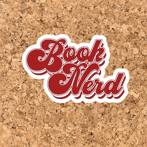 Può includere: Un adesivo rosso e bianco con il testo "Book Nerd" in uno stile di font retrò.
