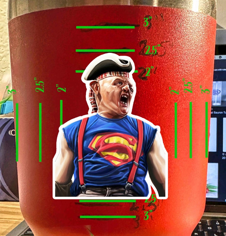 K&ouml;nnte beinhalten: Ein roter, rostfreier Becher mit einem wei&szlig;en Aufkleber eines Charakters aus dem Film 'Kevin - Allein zu Haus'. Der Charakter tr&auml;gt ein rot-blaues Hemd mit einem Superman-Logo, rote Hosentr&auml;ger und einen wei&szlig;en Piratenhut. Der Becher hat eine Messskala an der Seite mit Markierungen f&uuml;r 2,5 Zoll, 2 Zoll und 3 Zoll.