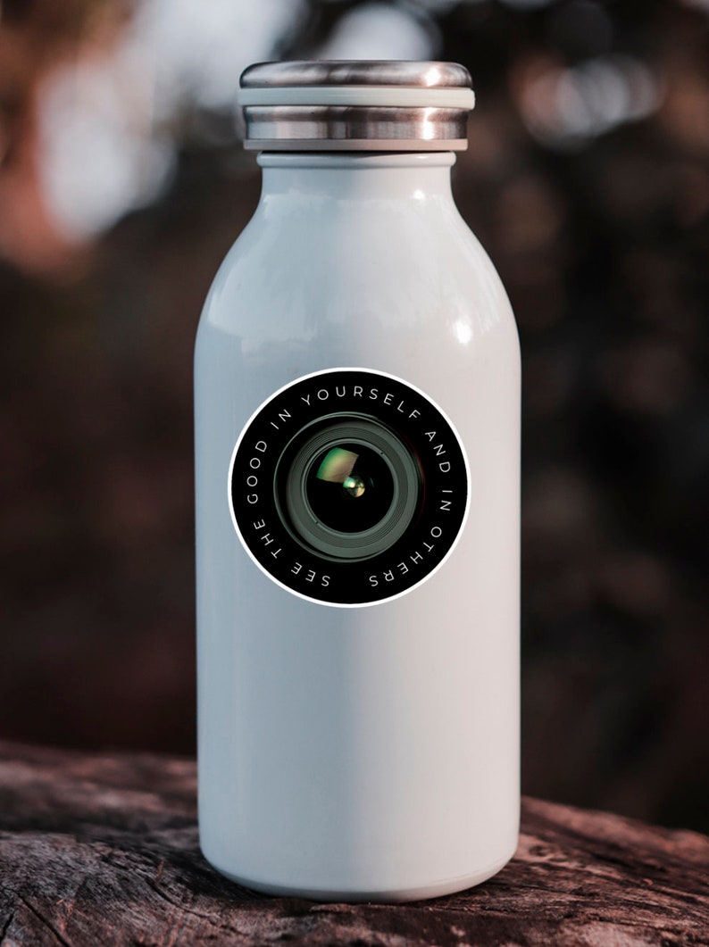 Puede incluir: Botella de agua de acero inoxidable blanca con una pegatina en blanco y negro que dice "See the good in yourself and in others" con un gr&aacute;fico de lente de c&aacute;mara.