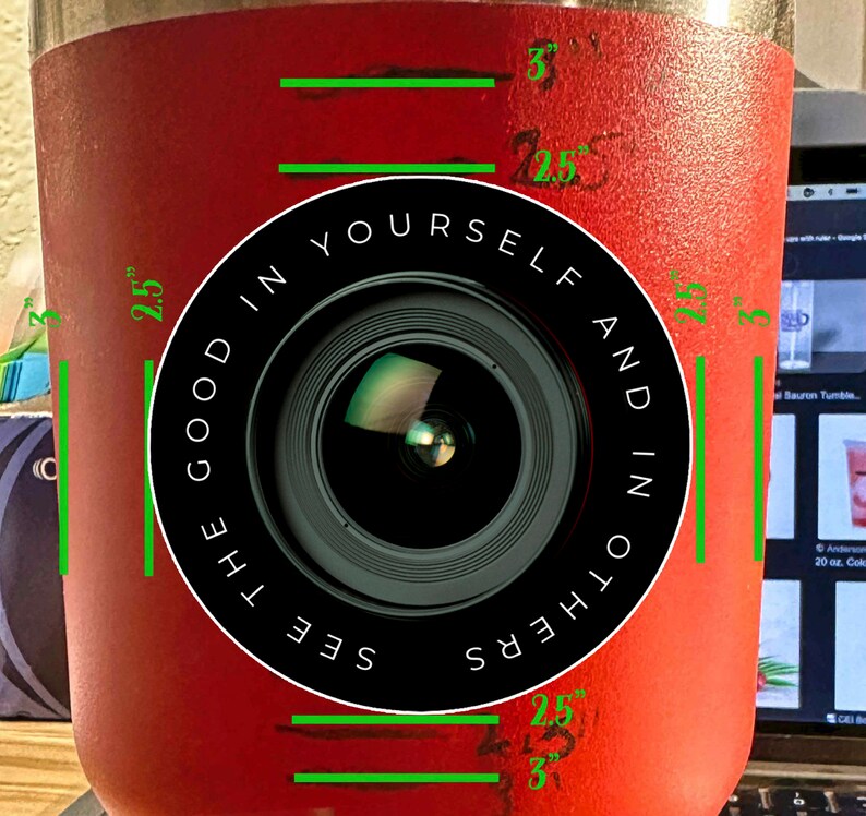 Puede incluir: Un vaso de acero inoxidable rojo con un dise&ntilde;o de lente de c&aacute;mara en blanco y negro. El texto "See the good in yourself and in others" est&aacute; impreso alrededor de la lente. El vaso mide 7,6 cm de alto y 6,4 cm de ancho.