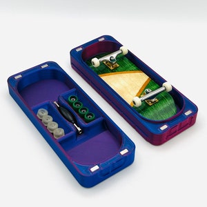 May include: A blue and purple fingerboard carrying case with a fingerboard and accessories. The case is open, revealing a fingerboard with a green and tan deck, and compartments with spare wheels and tools. The case is approximately 5 inches long.