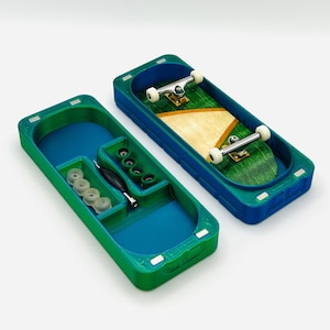 May include: A teal and green plastic storage case with a fingerboard skateboard inside. The case has a compartment for storing wheels and a tool.