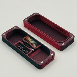 May include: A red and black storage box with a small glass vial and several small round objects inside. The box has the word "COFFEE" printed on the top.