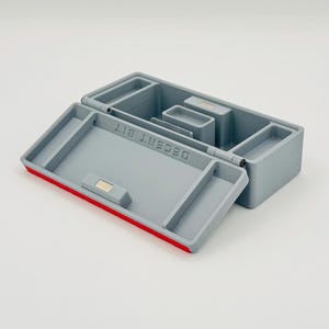May include: Gray plastic organizer box with a red trim and the text "DECENT BIT". The box is open, revealing several compartments of varying sizes. The box has a hinged lid and a magnetic closure.