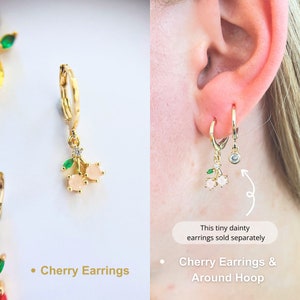 An pink cherr earrings hoop. The pink zirco on the cherry charm, decorated with a fresh green zirco leaf. 14K Gold-filled materials. These hoops exude elegance and playfulness, featuring designed cherry charms add a touch of tropical joy to ensemble.