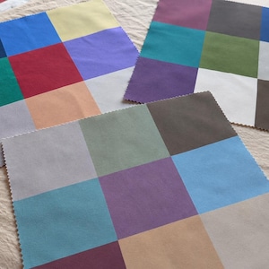 May include: Three square fabric swatches featuring a grid of nine distinct solid color blocks each. The swatches have pinked edges and display a variety of hues including blue, red, green, yellow, purple, gray, brown, and beige in different arrangements.