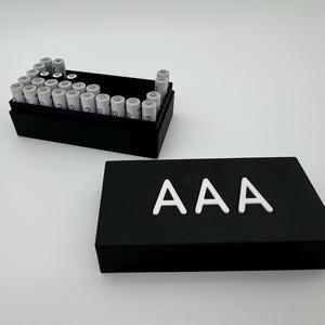 Könnte beinhalten: Eine schwarze Plastik-Aufbewahrungsbox mit einem weißen Etikett, auf dem "AAA" steht. Die Box ist geöffnet und mit AAA-Batterien gefüllt.