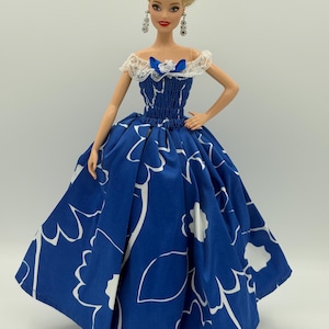 May include: A doll wearing a blue dress with a white floral pattern. The dress has a fitted bodice and a full skirt. The doll has blonde hair styled in an updo and is wearing dangling earrings.