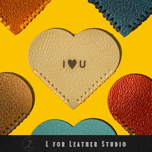 May include: Five leather heart-shaped tags in different colours, including brown, beige, red, blue, and teal. The beige heart has the words "I love you" embossed on it.