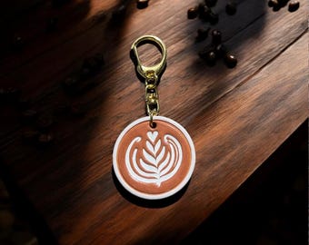May include: A brown and white leather keychain with a gold-colored ring. The keychain features a coffee art design with a heart and leaf pattern. The text "For Leather Studio" is at the bottom.