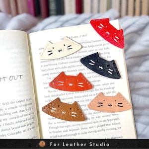 May include: Five leather cat-shaped bookmarks in different colors: red, cream, black, brown, and pink. Each bookmark has a stitched cat face with whiskers and a small 'W' on the forehead.
