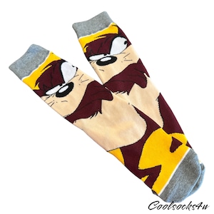 May include: A pair of grey and yellow socks featuring a cartoon image of a red and brown Tasmanian Devil. The socks have a white stripe at the top.