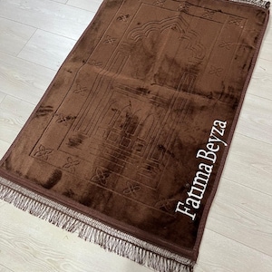 May include: A brown prayer rug with a fringe border and a white embroidered design of a mosque and the name "Fatma Beyza".