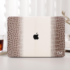 Op de afbeelding: Een laptophoes met een imitatie krokodillenleerpatroon in bruin- en crèmetinten. Het Apple-logo is zichtbaar. De initialen "TM" staan in de rechter benedenhoek.