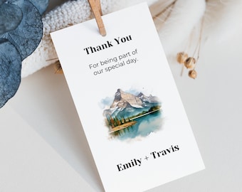 May include: White thank you tag with a watercolor illustration of a mountain range and a lake. The text reads "Thank You for being part of our special day. Emily + Travis"