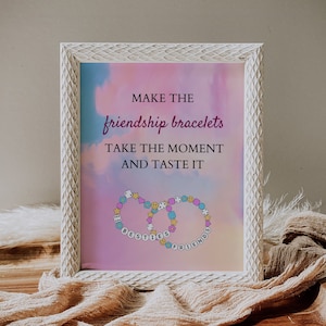May include: White framed print with a pink and blue watercolor background. The text reads "Make the friendship bracelets, take the moment and taste it". Two friendship bracelets are shown with the words "Besties" and "Friends" on them.