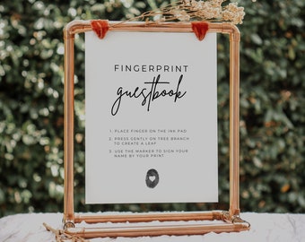 Pode incluir: Uma placa branca com o texto "FINGERPRINT guestbook" em fonte cursiva preta. A placa também inclui instruções para usar um livro de visitas com impressões digitais: 1. Coloque o dedo na almofada de tinta, 2. Pressione suavemente no galho da árvore para criar uma folha, 3. Use o marcador para assinar seu nome ao lado da sua impressão. A placa é exibida em um suporte de tubo de cobre.