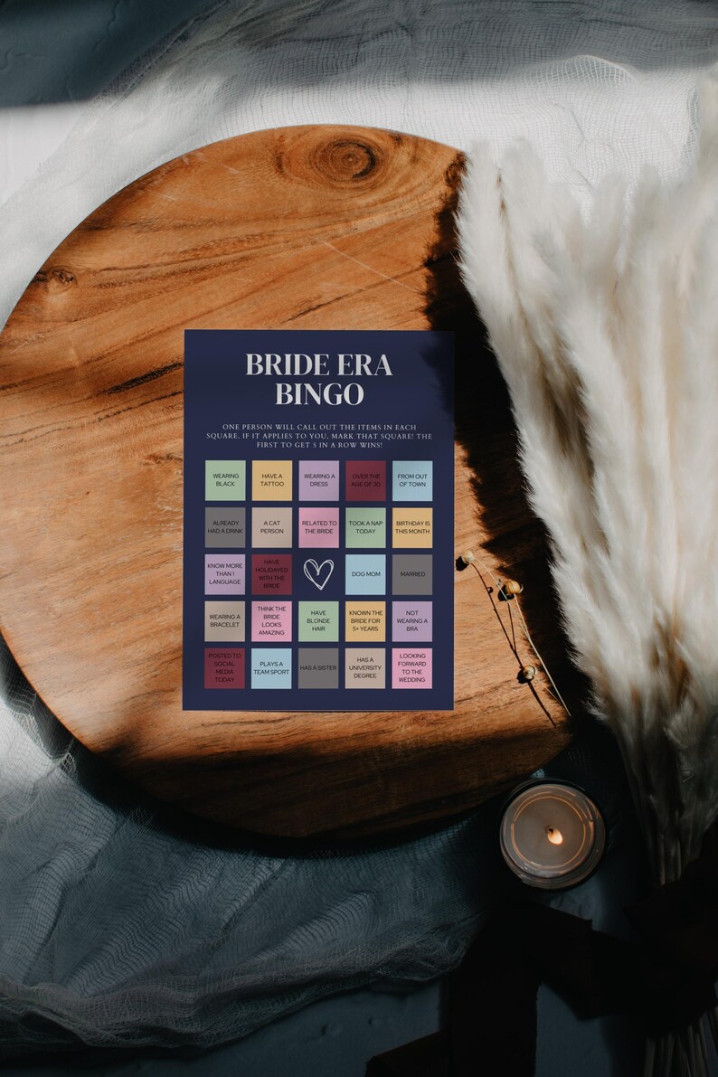 K&ouml;nnte beinhalten: Eine blaue und wei&szlig;e Bingokarte mit dem Titel "Bride Era Bingo". Die Karte hat 25 Felder mit verschiedenen S&auml;tzen, die mit einer Hochzeit zu tun haben, wie z. B. "Schwarz tragen", "ein Tattoo haben", "ein Kleid tragen", "gibt das Alter von", "ausserhalb der Stadt", "bereits ein Baby gehabt", "eine Katzenperson", "mit der Braut verwandt", "heute ein Nickerchen gemacht", "Geburtstag ist der Monat", "mehr als eine Sprache sprechen", "ein Armband tragen", "denke, dass die Braut toll aussieht", "blonde Haare haben", "die Braut seit &uuml;ber 5 Jahren kennen", "keinen Ring tragen", "die Braut heute kennengelernt", "einen Mannschaftssport spielen", "einen Master haben", "einen Hochschulabschluss haben", "sich auf die Hochzeit freuen".