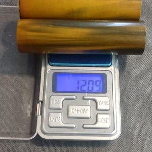May include: Two cylindrical wooden objects with a golden-brown hue are placed on a digital scale. The scale displays a weight of 120.9 grams. The objects have a natural wood grain pattern.