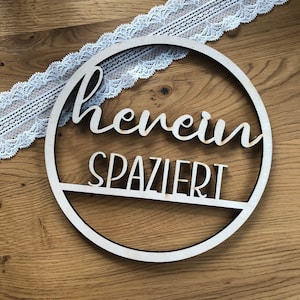 Könnte beinhalten: Ein Holz-Kreis mit den Worten "Herein Spaziert" darauf. Der Kreis ist mit weißer Spitze verziert.