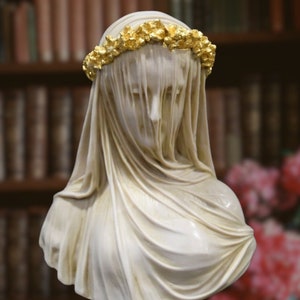 May include: White marble bust of a woman wearing a veil and a gold leaf crown. The bust is on a gold leaf base. -DECORAR CON ARTE-