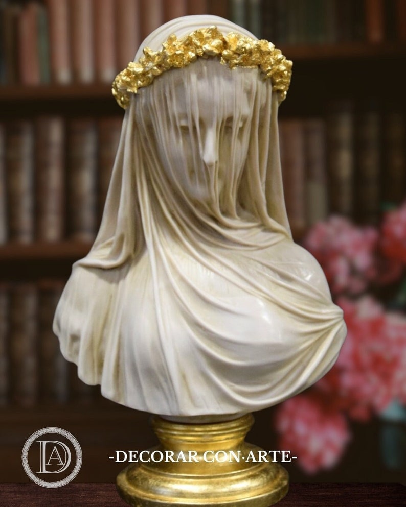 May include: White marble bust of a woman wearing a veil and a gold leaf crown. The bust is on a gold leaf base. -DECORAR CON ARTE-