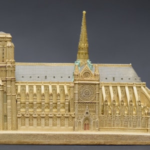 May include: A detailed miniature replica of Notre Dame Cathedral in Paris, France. The model is made of a light brown material and features intricate details, including the iconic rose window and twin towers.