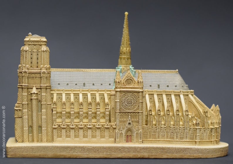 May include: A detailed miniature replica of Notre Dame Cathedral in Paris, France. The model is made of a light brown material and features intricate details, including the iconic rose window and twin towers.