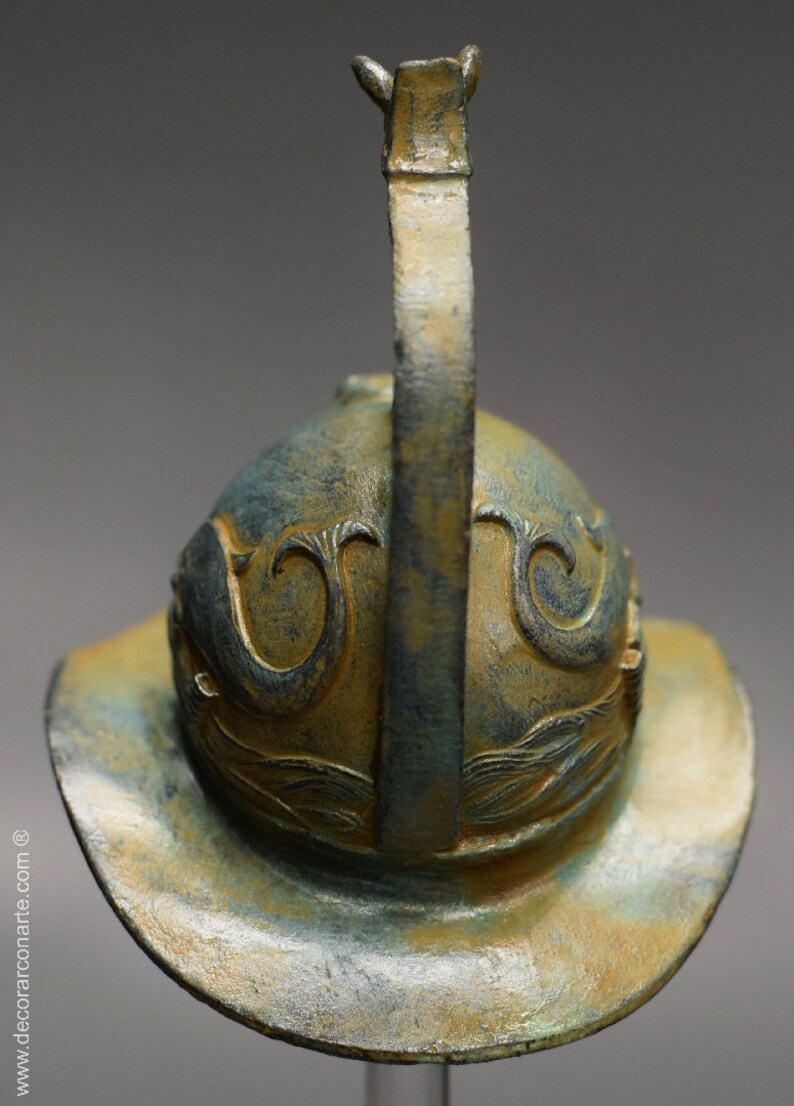 May include: A bronze helmet with a decorative design and a tall, curved crest. The helmet is a dark green and gold color.